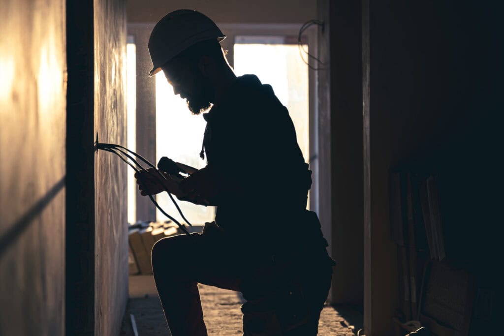 A construction electrician cuts a voltage cable during a repair, silhouette in the light of the setting sun.